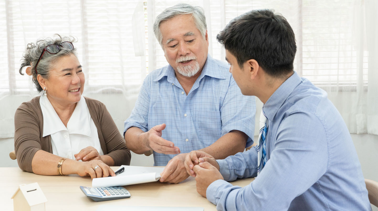 Conseillère de résidence senior présentant documents budgétaires à une famille (adulte et parent âgé) dans un bureau accueillant
